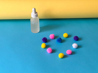 Serum in a transparent bottle on a blue and yellow background with a pom-pons folded in the shape of a heart