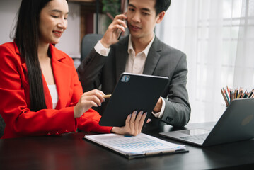 Asian business colleague business presents and explains and using laptop and tablet. Teamwork, financial marketing team,   while sitting in modern office