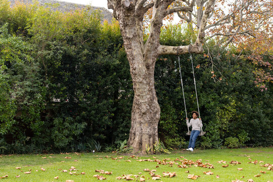 Happy african american boy swinging on tree swing in garden, copy space