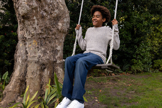 Happy african american boy swinging on tree swing in garden