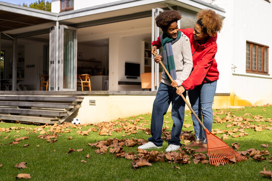 Happy african american mother and son raking leaves in garden