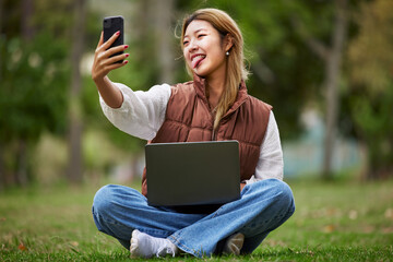 Selfie, asian and woman student in a park to update social media while outdoor studying and learning online. Internet, web and young person or influencer takes picture in nature for peace and calm