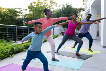 Happy african american couple with son and daughter practicing yoga on sunny terrace at home