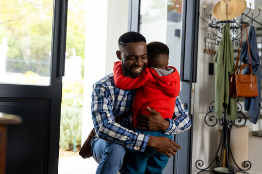 Happy african american father hugging son in front door at home