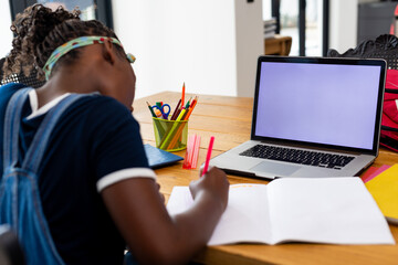 Back of african american girl learning online using laptop with copy space on screen at home