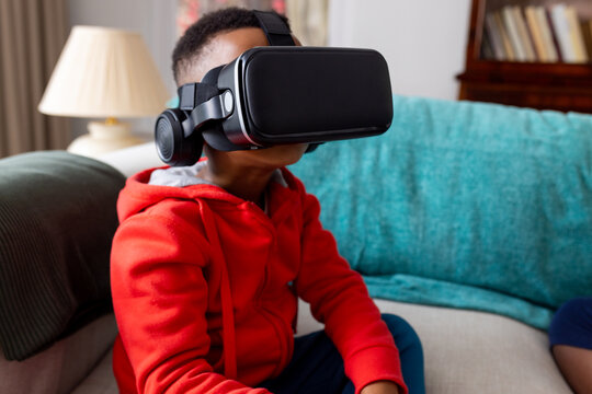 Happy african american boy using vr headset on sofa at home