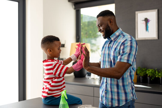 Happy african american father and son high fiving in kitchen at home