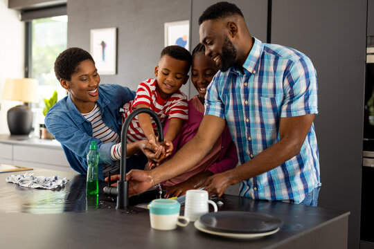 Happy african american couple with son and daughter washing dishes in kitchen at home
