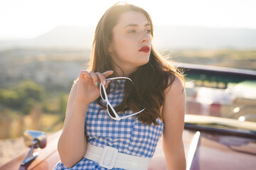 beautiful girl in a retro dress and sunglasses at sunrise happy posing on the background of the...