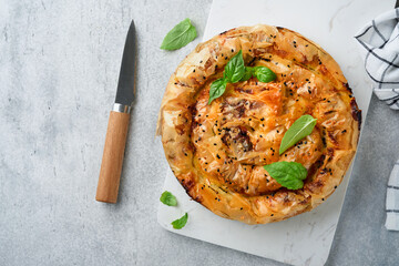 Delicious pie Spanakopita with soft feta cheese and spinach on old gray concrete table backgrounds. Traditional Greek Spiral filo pastry pie spanakopita in shape of roll. Traditional Greek cuisine.