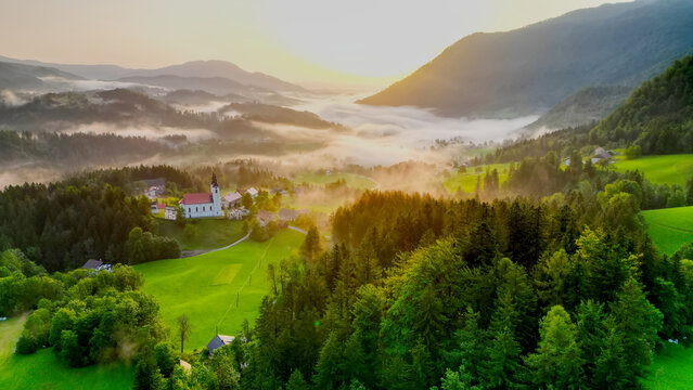 Aerial drone view of small beautiful church on valley in Slovenia at dawn. Beautiful summer morning landscape.