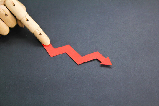 finger holding a red arrow pointing down. the concept of devaluation. The concept of reducing costs and profits, falling living standards and prices. Decreased projections, depressed economies.