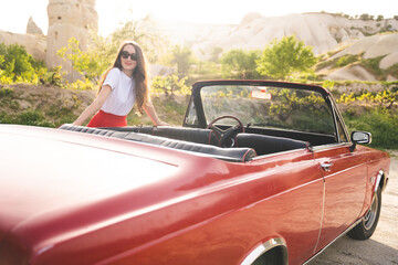 beautiful happy girl in a skirt posing near a retro car in the mountains of cappadocia