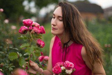 a beautiful girl in a pink dress is picking red roses in the garden