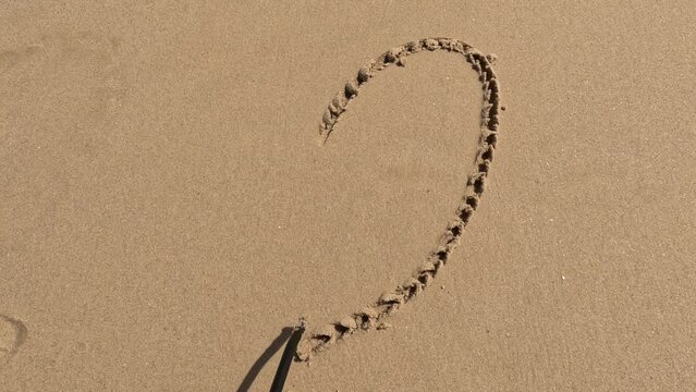 Message I love you on the sand with hand drawing on the beach .drawing a heart on the sand with a stick.