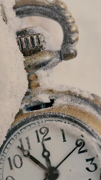 Close up antique pocket watch thrown in the snow, while the hands make their way quickly.  Vertical shot.