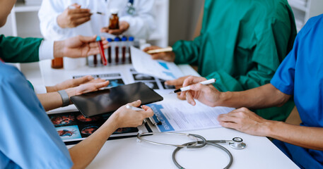 Medical team having a meeting with doctors in white lab coats and surgical scrubs seated at a table...