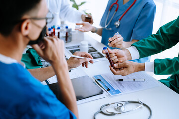 Medical team having a meeting with doctors in white lab coats and surgical scrubs seated at a table discussing a patients working online using computers