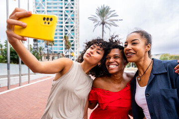 Three mixed race hispanic and black women bonding outdoors and taking a selfie for social media wiyh mobile phone