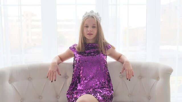 Portrait of a cute little princess with a crown on her head. The girl winks and smiles at the camera.