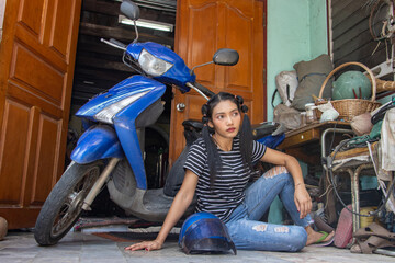 Plakat A young woman is sitting by a motorcycle parked in front of the entrance to a house
