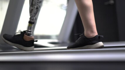 Woman with prosthetic leg using walking on a treadmill while working out in the gym.