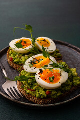 Sandwiches with rye bread and guacamole, with boiled eggs and microgreens of peas and radishes and sesame seeds, a plate with sandwiches close-up on a green background