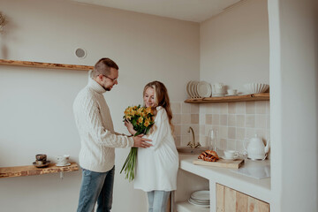 Beautiful pregnant couple in kitchen with bouquet of flowers