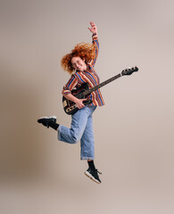 Joyful female musician with guitar jumping ecstatically in mid-air against background