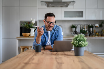Cheerful businessman having a phone call on speakerphone with client, wearing eyeglasses in home...