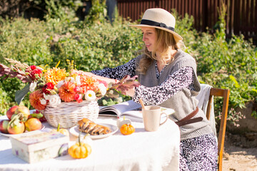 A cute girl in a straw hat is sitting at a picnic table outside, reading a book