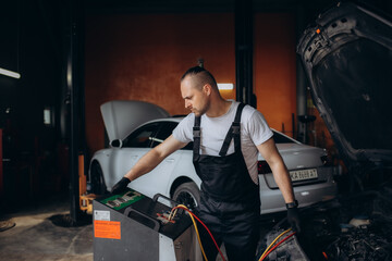 Car mechanic with manometer to fill the gas in the car air conditioning compressor. Service of checking the car air conditioner. Refrigerant recharge system.