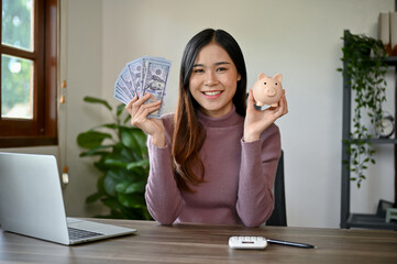 Young smiling Asian woman saving her money by using Piggy Bank.