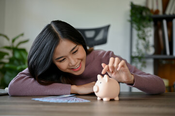 Obraz na płótnie Canvas Young smiling Asian woman saving her money by using Piggy Bank.