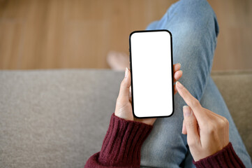 A young girl using blank screen mock up smartphone while sitting in the sofa
