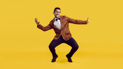 Fototapeta na wymiar Happy funny young man dancing isolated on yellow colour background. Full body shot of handsome positive goofy confident ethnic guy in leopard party jacket with bowtie dancing and having fun in studio