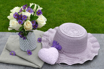Romantische Dekoration: Blumenstrauß mit Herz und einem Hut auf einem Tisch im Garten, mit Platz für Text.