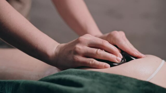 Young woman having hot stone massage for legs and buttocks in spa salon. Close-up. 
