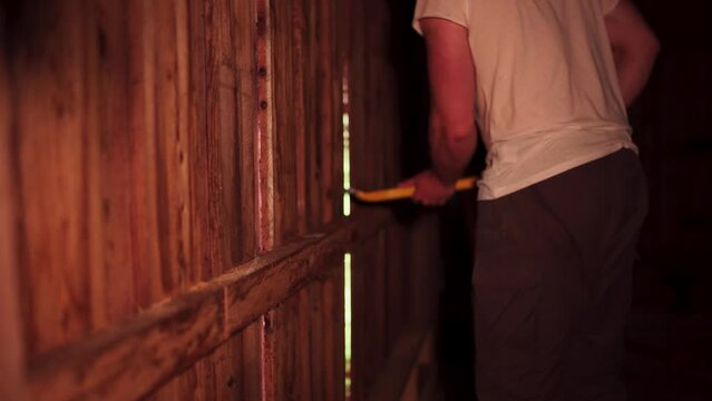 Cropped View Of A Man Dismantling Wooden Plank Walls Of A Barn House Using Crowbar. Close Up