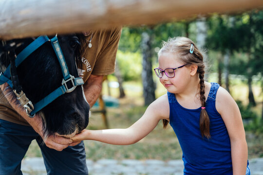 Little brown haired girl feeding and stroking a pony horse outdoor. Concept of hippotherapy, therapy, trust, outdoor activity, equestrian club, psychology, relax, hobby.
