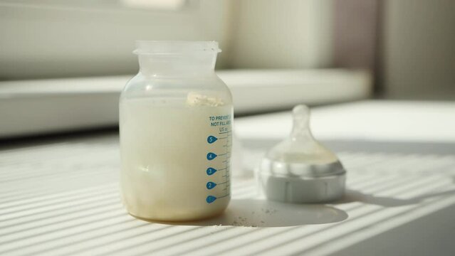 Pouring milk formula into a baby bottle with water for preparing baby food, close-up.