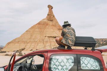 Traveler sitting on top of a van taking photos of the rocky landscape of the Navarra desert