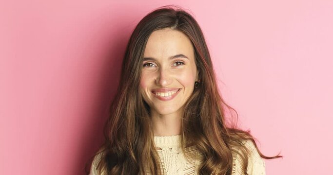 Playful happy contented brunette woman wear knit sweater blinking eye, looking at camera with toothy smile, winking and flirting, expressing optimism. Indoor studio shot isolated on pink background