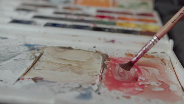 Brush is dipped in watercolor paints and color is mixed on a palette