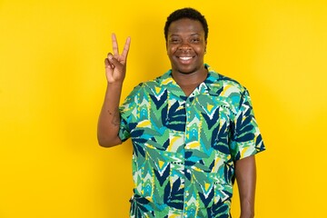 Young latin man wearing hawaiian shirt over yellow background showing and pointing up with fingers number two while smiling confident and happy.