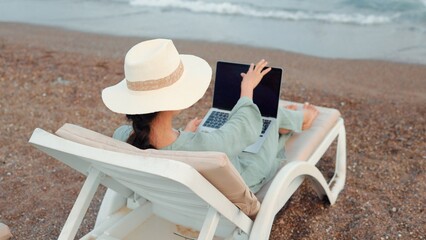 Rear view of freelancer woman working on laptop near the sea. Remote work concept. work on vacation. 4 k