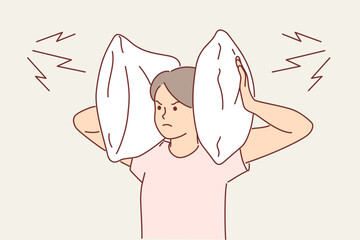 Irritated woman covers ears with pillow so as not to hear noise from neighbors who are having party