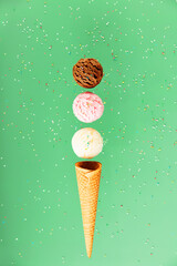 Chocolate, vanilla, strawberry scoops and waffle cone on green background with colorful sprinkles, levitating concept