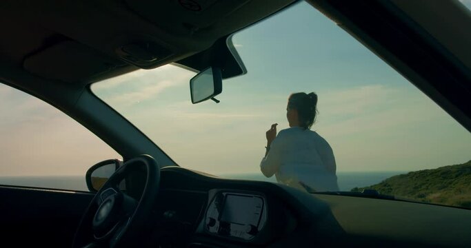 Woman dancing next to car during sunset, view from inside car
