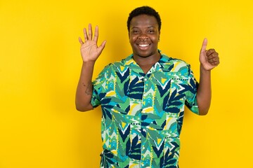 Young latin man wearing hawaiian shirt over yellow background showing and pointing up with fingers number six while smiling confident and happy.